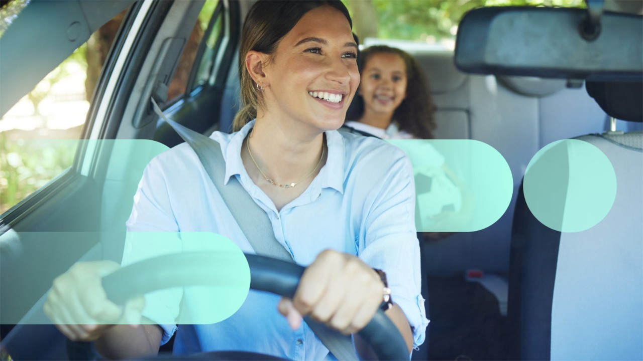 A parent and child smiling at each other in a car. The parent is in the driver's seat and the child is in the backseat.