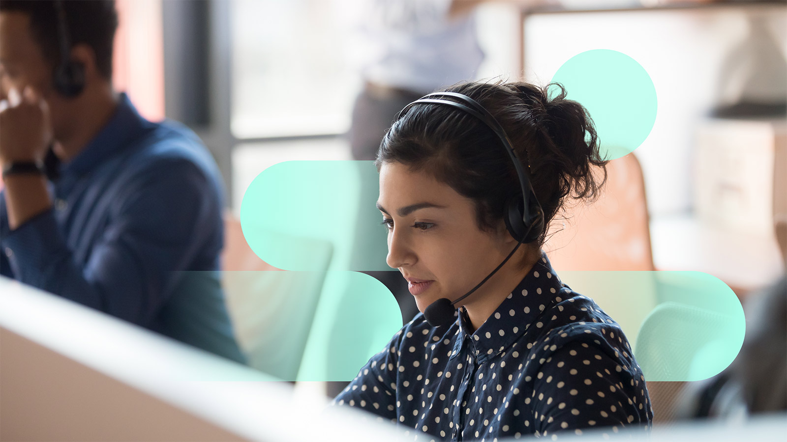 A person in business clothes wearing a headset, while sitting at a desk. 