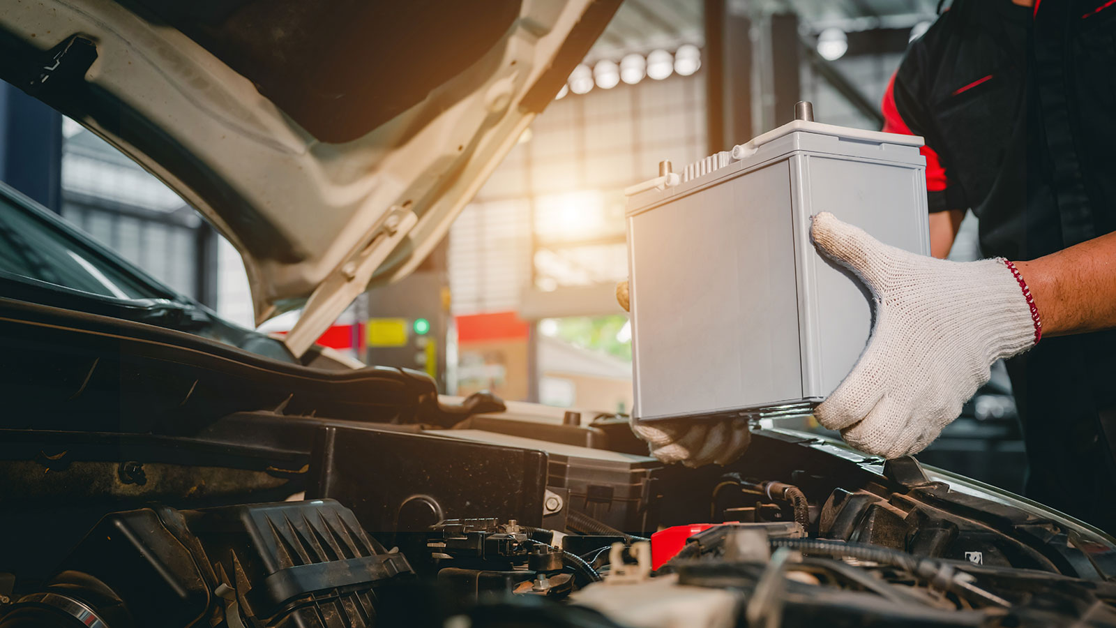 A tradesperson holding a battery over an open car bonnet.