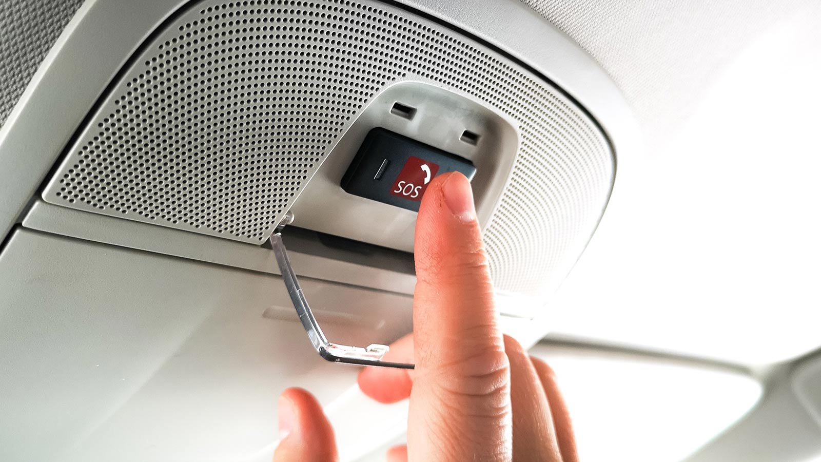 A hand reaching for the SOS button on the ceiling of their car.