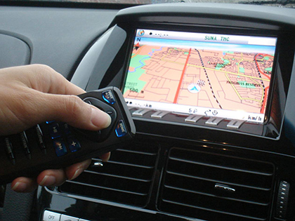 Hand pointing a remote at a car's in-built infotainment screen, which shows a GPS.