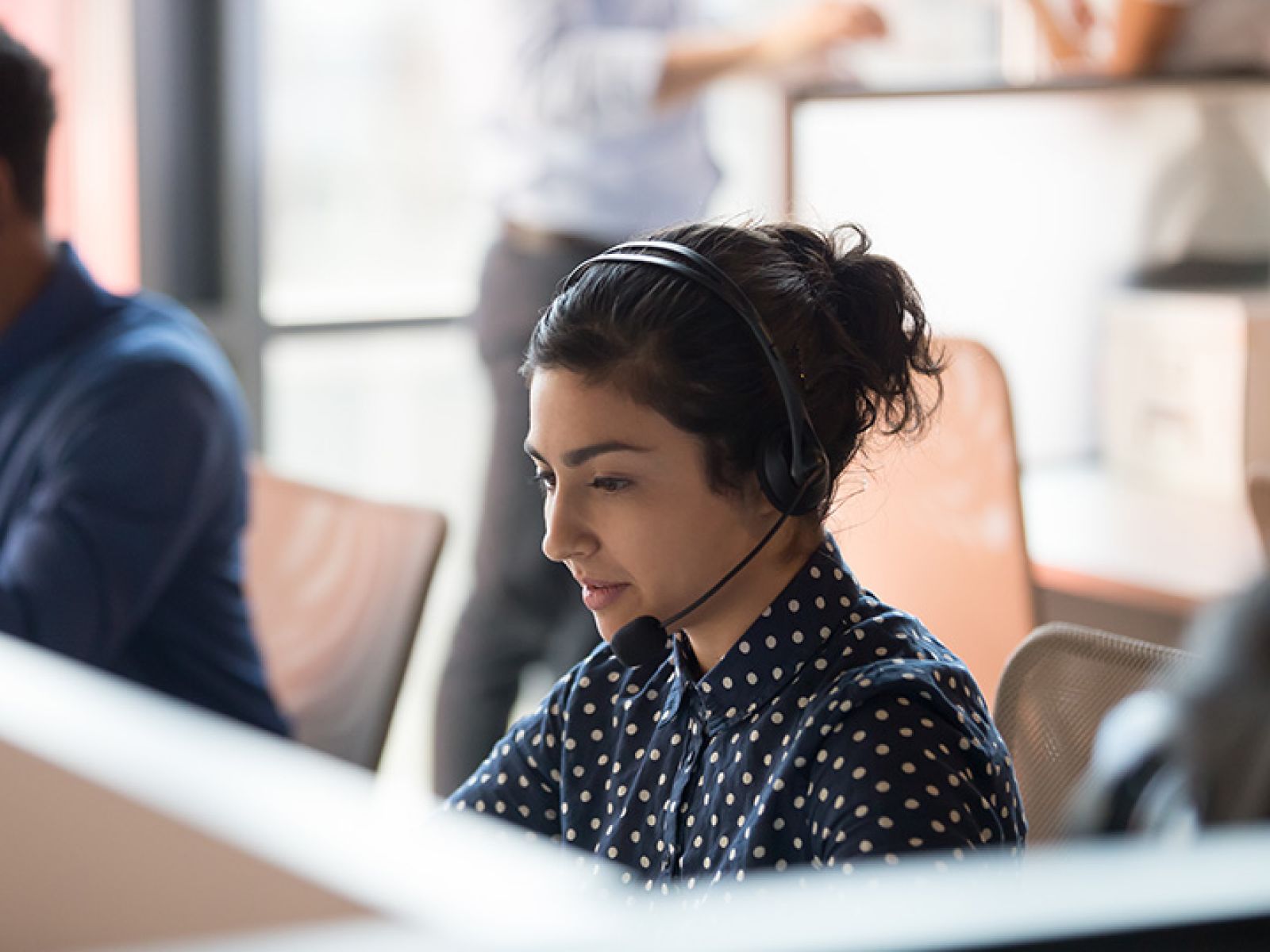 A person in business clothes wearing a headset, while sitting at a desk. 