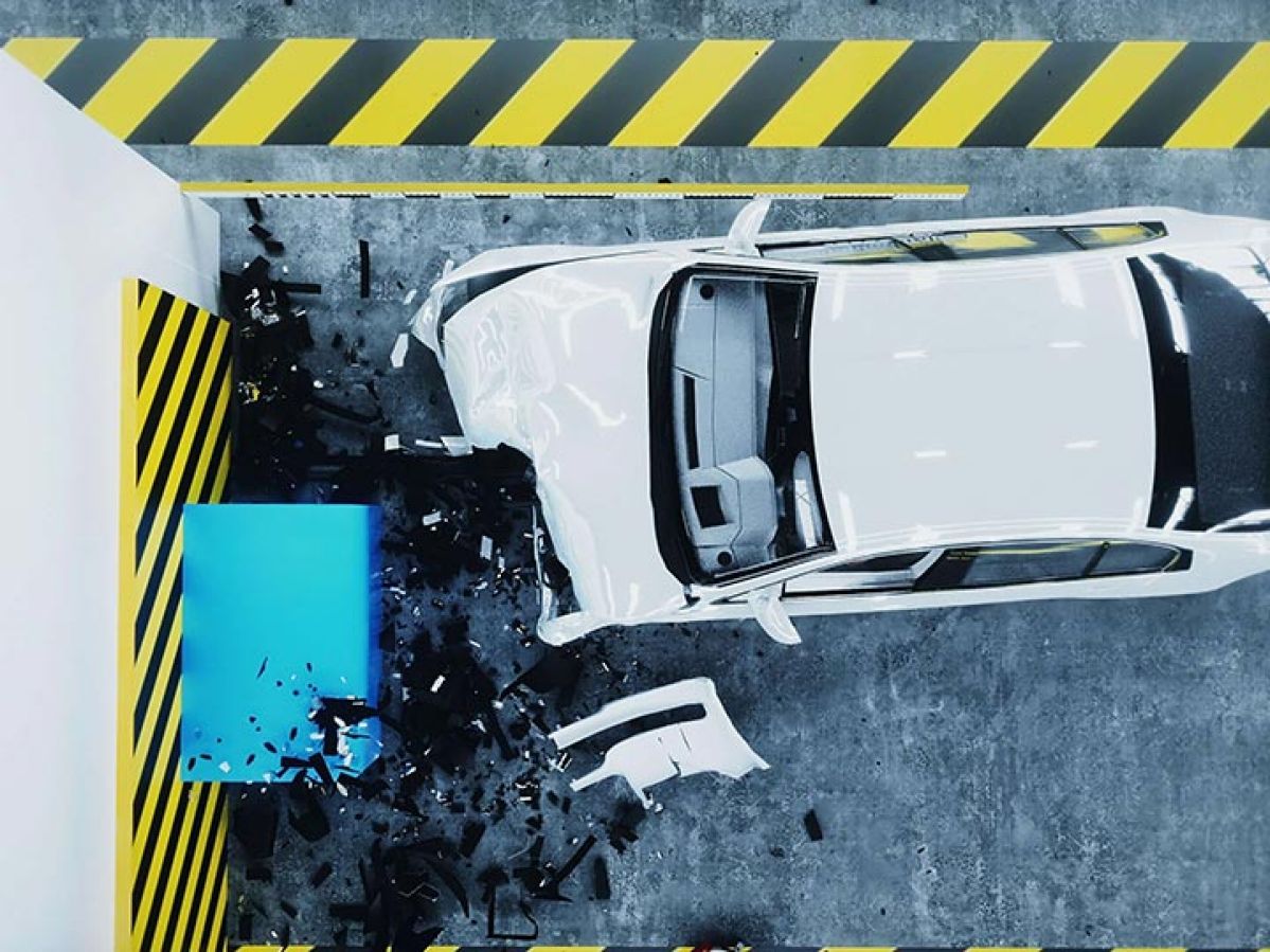 A crashed white car in a warehouse, with the front crumpled and surrounded by debris. The car is surrounded by yellow and black tape.
