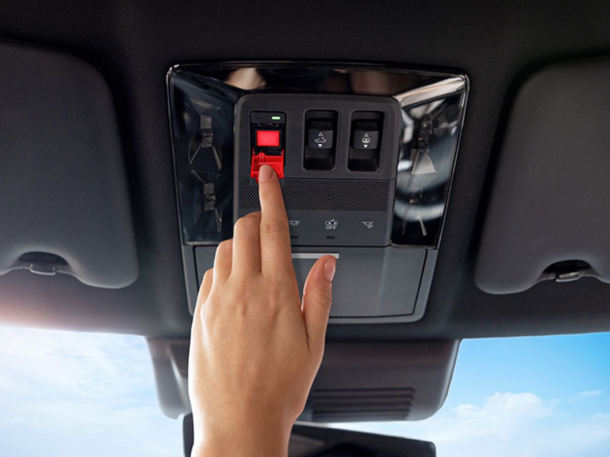 A hand reaching for the SOS button on the ceiling of their car.