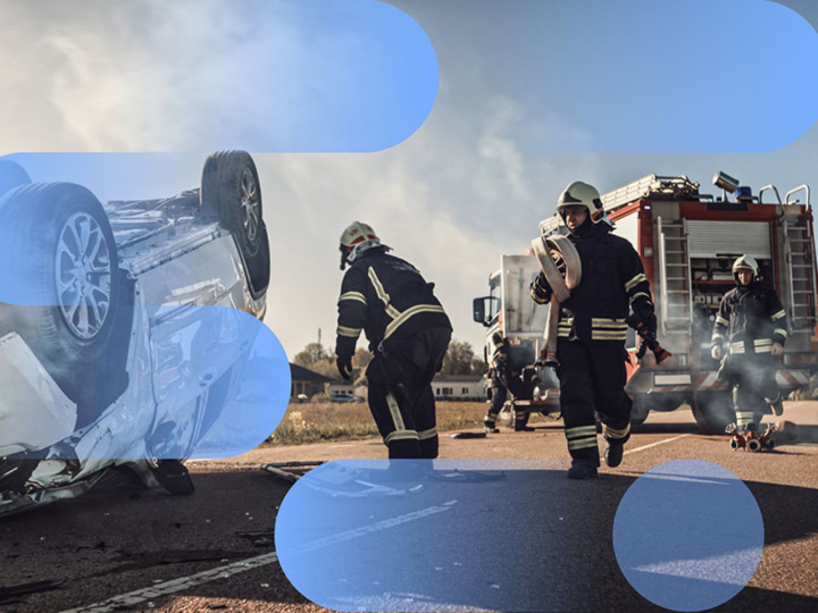 Firefighters exiting a fire truck and walking towards a crashed, upside down white car on the side of the road.