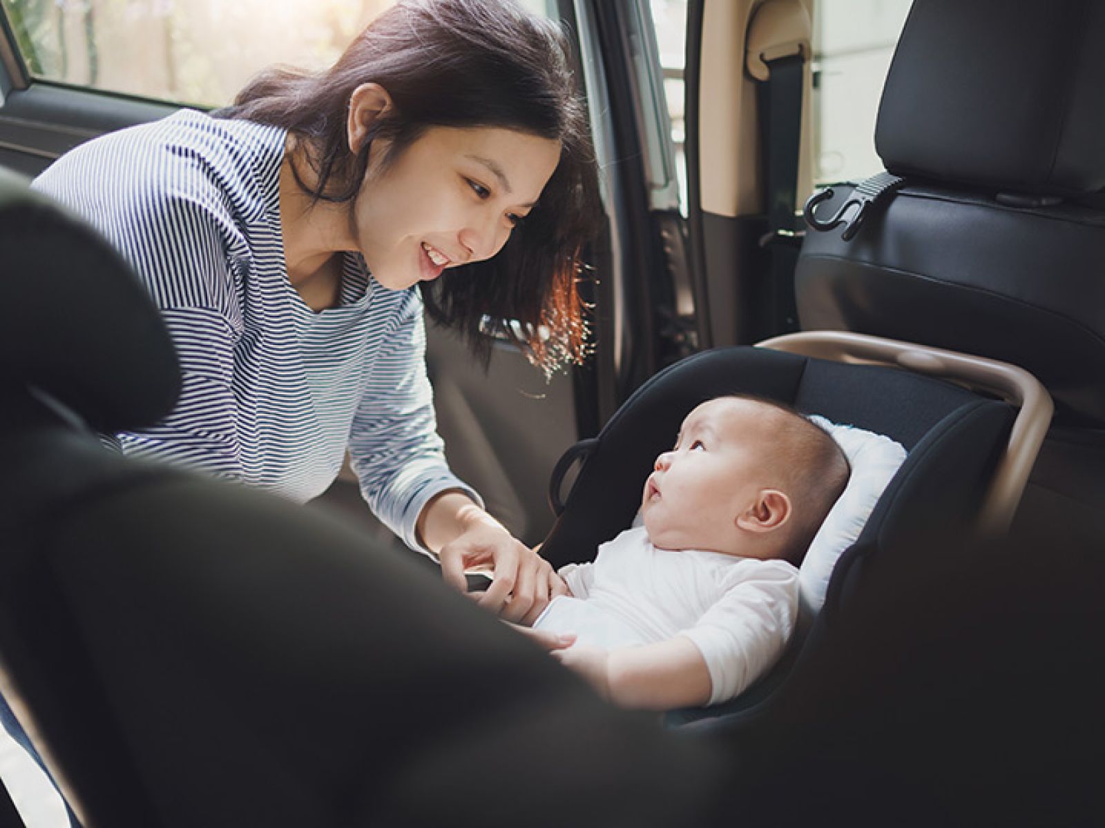 A parent smiling at their infant, who is in a baby car seat.