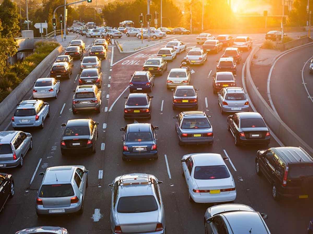 Six traffic lanes full of cars at an intersection during sunset. The first 2 lanes turn left while the other 4 lanes go straight. The far left lane going straight is a bus lane.