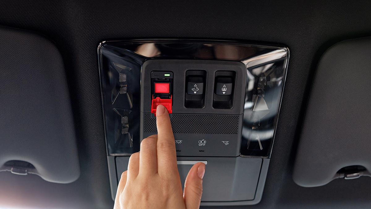 A hand reaching for the SOS button on the ceiling of their car.