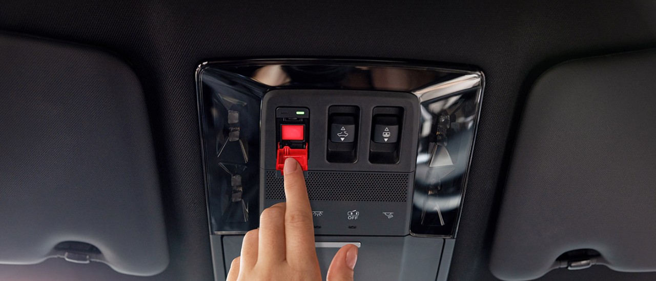 A hand reaching for the SOS button on the ceiling of their car.
